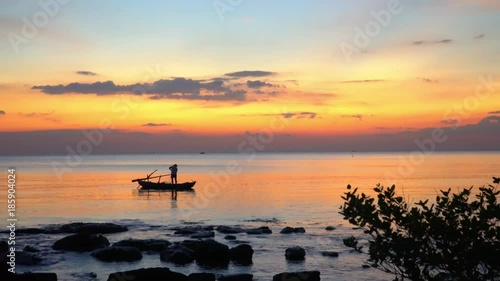 A silhouette of the small boat with the fisherman at sunset. Boat on open sea sunset horizon. Beautiful yellow decline on the ocean horizon. Ph Qu c Island.