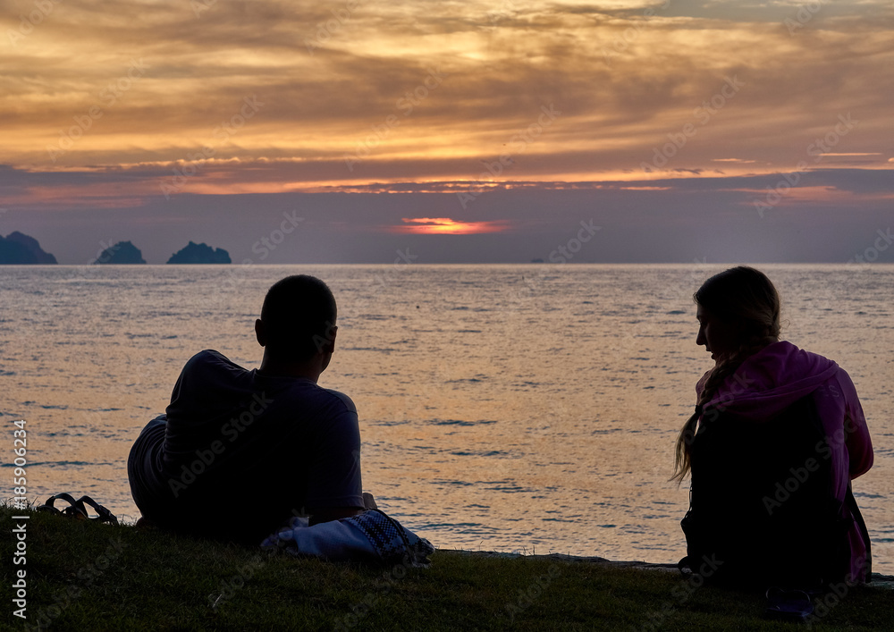 Young couple sitting on the beach and watching sunset
