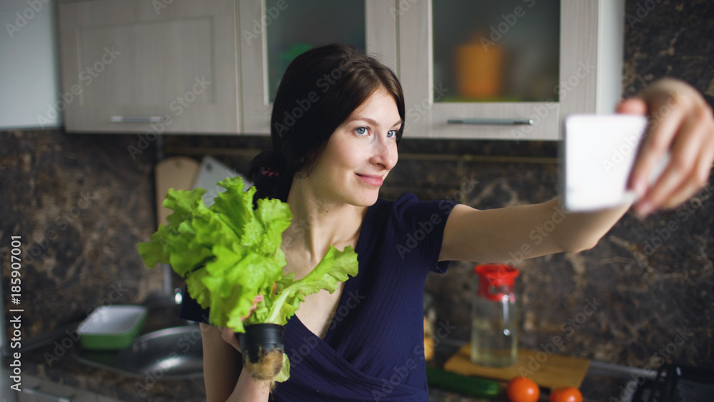 Funny woman housewife shoot selfie with green salad while cooking in the kitchen at home indoors Funny woman housewife shoot selfie with green salad while cooking in the kitchen at home indoors