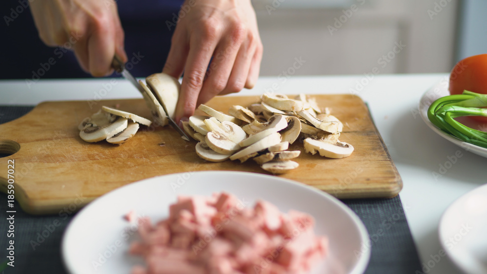 Closeup of girl hands cutting the mushrooms on wooden board for pizza in the kitchen at home Closeup of girl hands cutting the mushrooms on wooden board for pizza in the kitchen at home