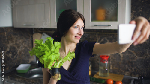 Funny woman housewife shoot selfie with green salad while cooking in the kitchen at home indoors