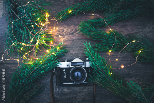 The old camera on a wooden background with Christmas tree branches and lights.