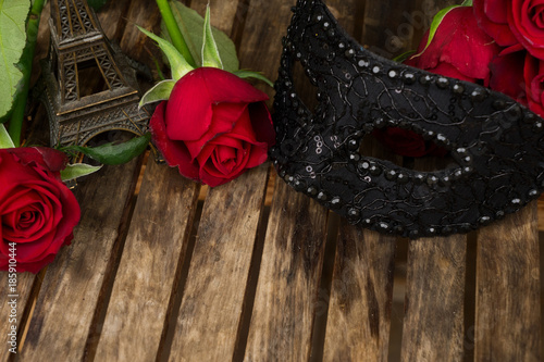 red fresh roses with masque and eiffel tower on wooden table photo