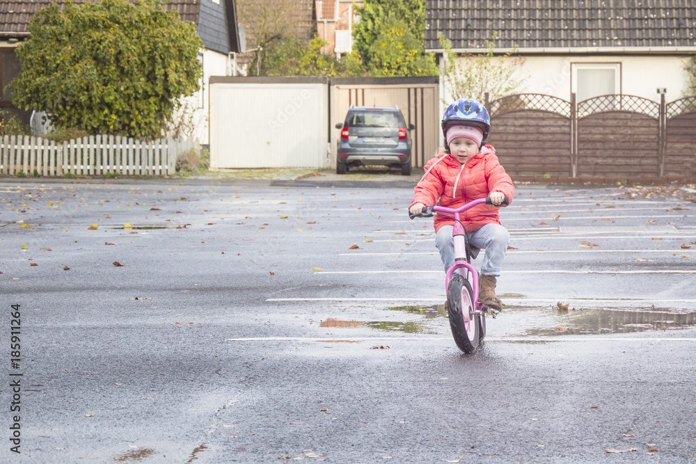 Fototapeta premium Happy child riding a bicycle in the fall. Cute little girl in safety helmet riding a bike outdoors. Little girl on a red bicycle. Healthy preschool children activity.