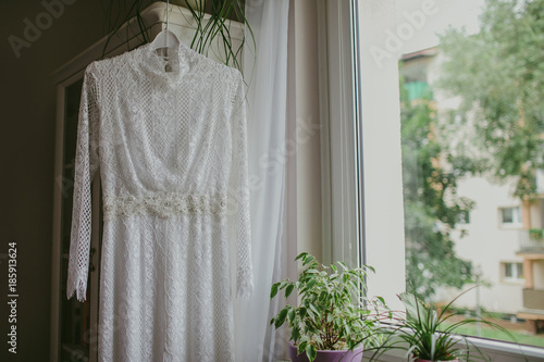 White wedding dress hanging on wardrobe next to the window.