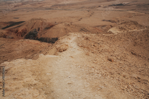 Dry desert hiking trail on the mountain slope. Panoramic view of Negev desert in Israel.
