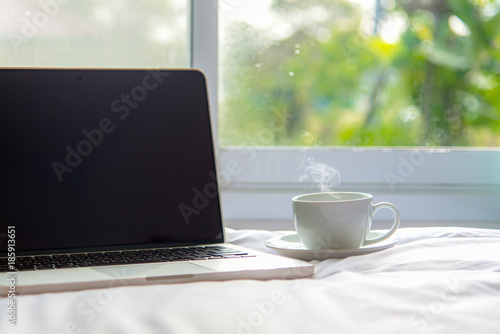 The laptop working on the white bed and coffee in the window on rainy day, Fresh morning holiday. Lifestyle Concept. soft and select focus.