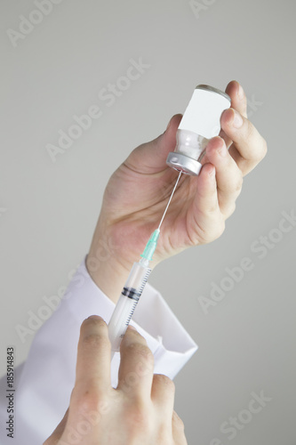 Hands in gloves filling medicine from ampule into syringe against the background of medical robe. photo