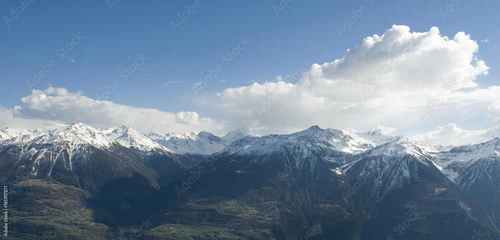Obraz premium Landscape of mountains of a strong spring green, with snow-covered peaks after a strong thunderstorm, fresh snow, green and yellow grass, sun, light, white clouds, alps, Switzerland