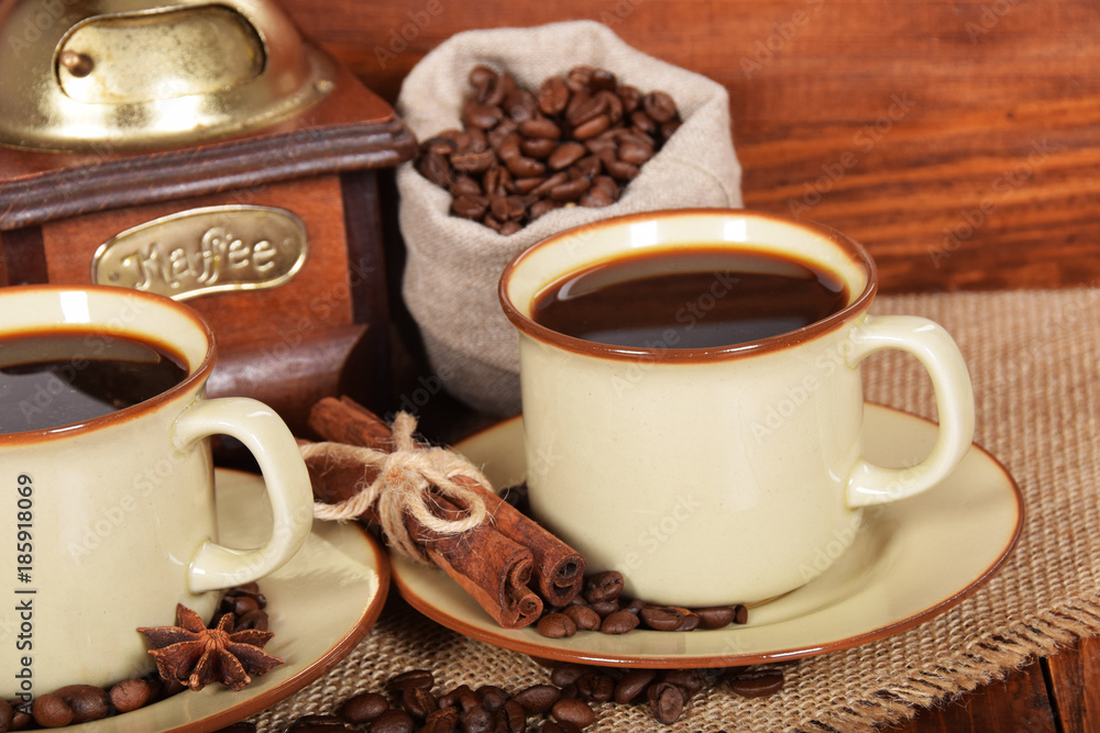 coffee beans in a gray bag next to a coffee grinder and two cups of hot coffee