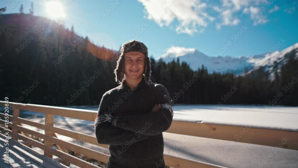 Closeup Winter Portrait of a Self-Confident Young Man in Ear Flapped Fur Hat Looking at Camera with Beautiful Mountains and Snow at Background with Sun Lense Flare Closeup Winter Portrait of a Self-Confident Young Man in Ear Flapped Fur Hat Looking at Camera with Beautiful Mountains and Snow at Background with Sun Lense Flare