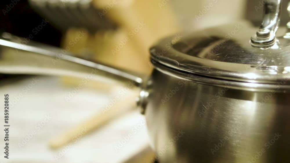 Steam rolls from under the lid of a covered pot on the stove with roll focus Steam rolls from under the lid of a covered pot on the stove with roll focus