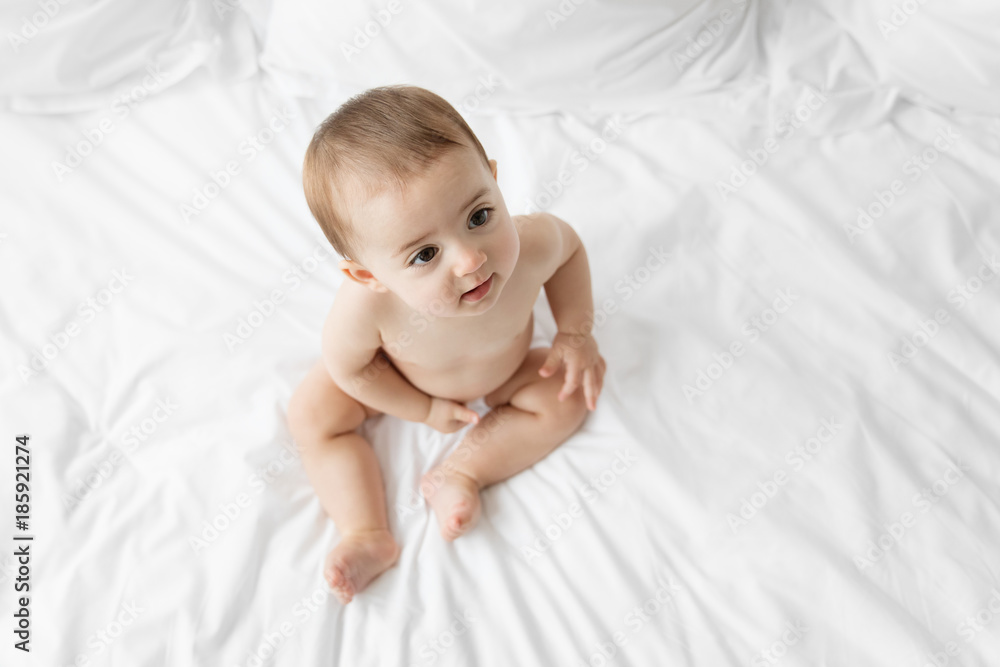 High angle of baby girl looking up while sitting on the bed High angle of baby girl looking up while sitting on the bed