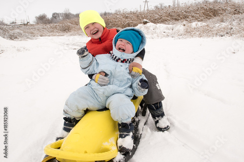Two brother's boys are having fun riding a new yellow sled. Children, best friends are happy on a winter day. Active rest with children. Casual boy's fashion