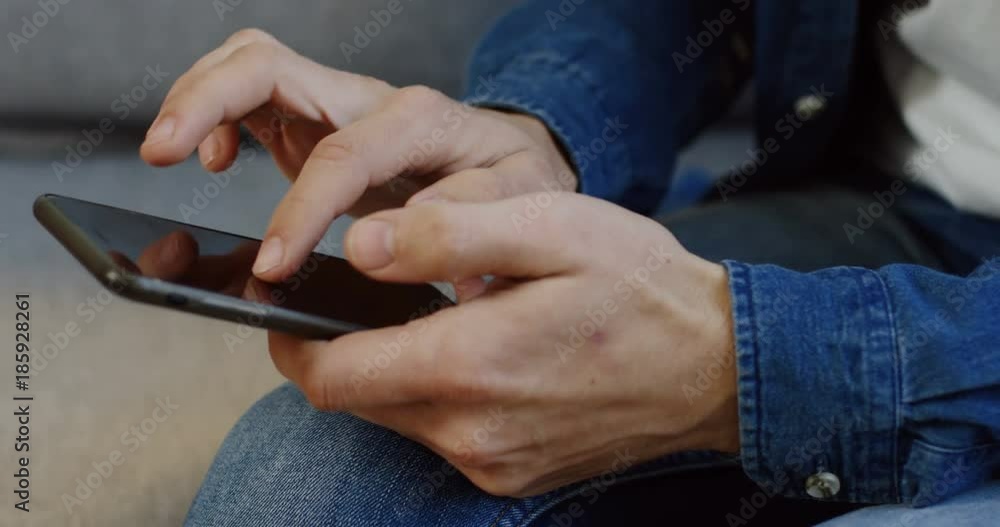 Close up of the Caucasian male hands with jeans sleeves scrolling, taping and zooming on the black smartphone screen. Inside Close up of the Caucasian male hands with jeans sleeves scrolling, taping and zooming on the black smartphone screen. Inside