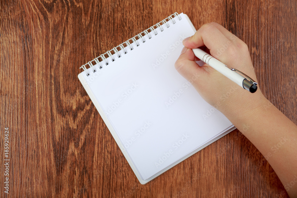 Top view of blank notebook and woman hand with pen, free space. Girl writing letter, copy space. Flat lay on wooden background Top view of blank notebook and woman hand with pen, free space. Girl writing letter, copy space. Flat lay on wooden background