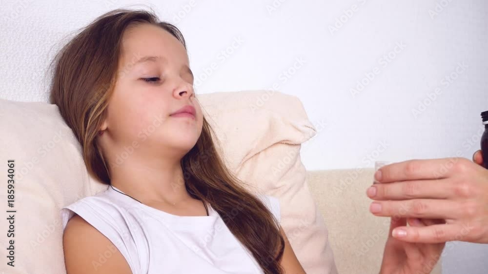 Mother or doctor giving medicine syrup to her sick daughter in bed Mother or doctor giving medicine syrup to her sick daughter in bed