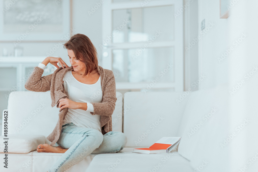 young woman in her late twenties sitting and laying on a lether white sofa in a cosy interier of her bright home and drinking a cup of tea and reading a book, totaly relaxed young woman in her late twenties sitting and laying on a lether white sofa in a cosy interier of her bright home and drinking a cup of tea and reading a book, totaly relaxed