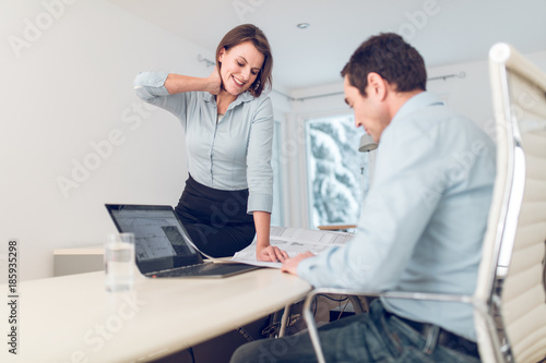 Young beautiful woman and her co-worker in an office, discussing an architecture project behind their desk and talking