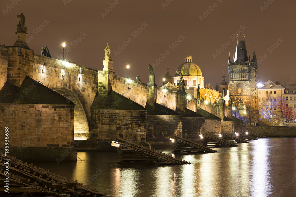 Night snowy Prague Old Town with Bridge Tower and St. Francis of Assisi Cathedral and Charles Bridge with its baroque Statues, Czech republic