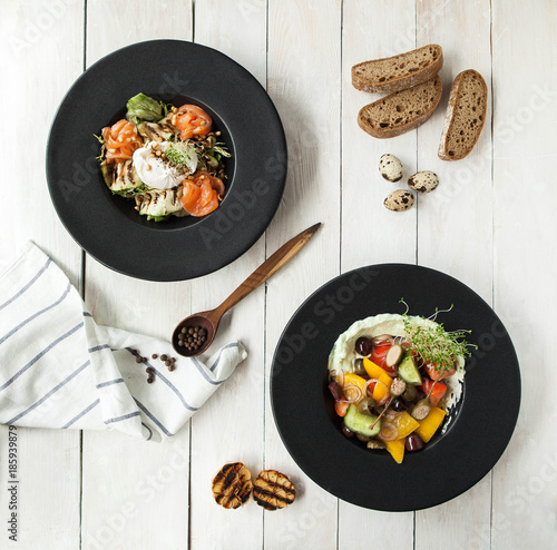 Salad with fresh salmon, grilled zucchini and poached eggs and a plate of hummus and vegetables on a white wooden table photo