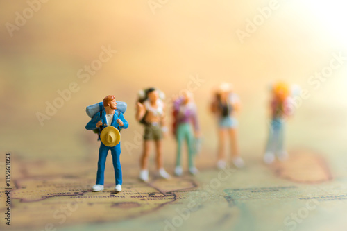 Miniature people: travelers with backpack standing on world map, walking to destination.