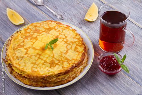 Stack of thin pancakes, crepes on white plate, cup of tea and berry jam