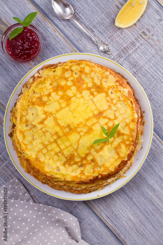 Stack of thin pancakes, crepes on white plate, cup of tea and berry jam, overhead Stack of thin pancakes, crepes on white plate, cup of tea and berry jam, overhead