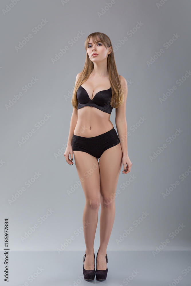 Flawless woman in black bikini on grey background. Photo of girl with slim toned body. Beauty and body care concept Flawless woman in black bikini on grey background. Photo of girl with slim toned body. Beauty and body care concept