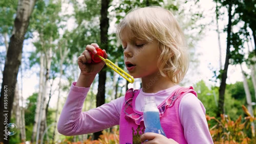 The cute little blonde girl blowing soap bubbles in the summer park. 4K The cute little blonde girl blowing soap bubbles in the summer park. 4K