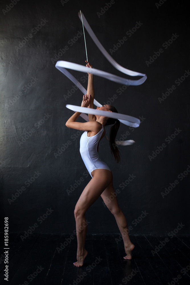 Beautiful woman gymnast with a white ribbon on a black background.