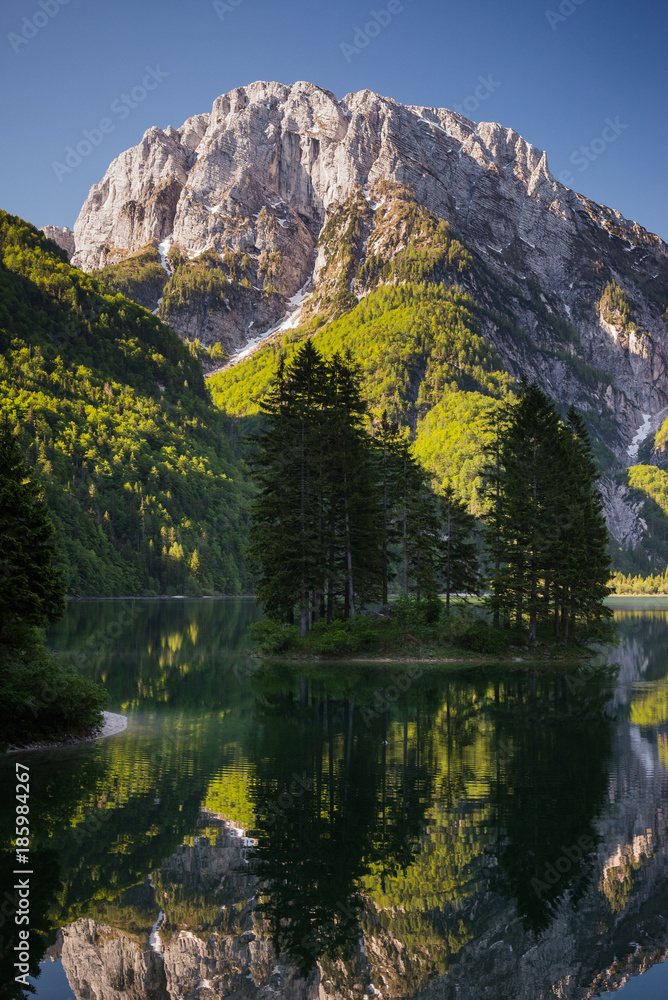 Vertical photo of reflections in Lago del Predil in the morning in Tarvisio municipality in Italy