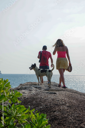 Couple and dog walking on the rock looking on the sea
