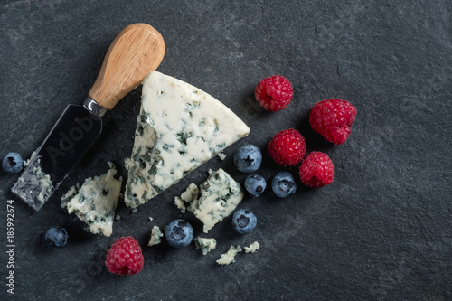 Blue cheese with fresh berries on stone dark black background. French food concept. Top flat view, from above.