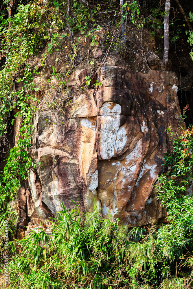 Stone face of Buddha by the Picturesque road in mountains of National park Bokor leading to Abandoned hotel Bokor Palace in Ghost town Hill station near Kampot. Cambodia Stone face of Buddha by the Picturesque road in mountains of National park Bokor leading to Abandoned hotel Bokor Palace in Ghost town Hill station near Kampot. Cambodia