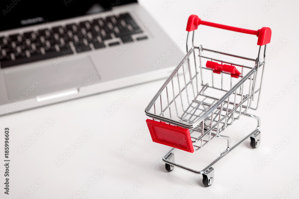 Online shopping. Bank card nearby a laptop and mini shopping cart on white background top view.