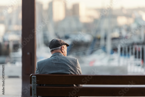 Hombre adulto irreconocible sentado en un banco frente al puerto photo