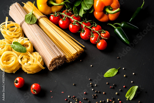 Raw italian pasta.Spaghetti and fettuccine with tomatoes, vegetables, herbs and pepper on a black background . Closeup.
