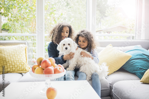 Sisters sitting on couch, petting little whit dog