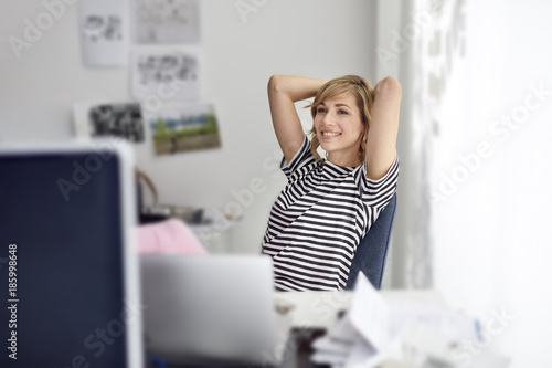 Portrait of smiling blond business woman with laptop, leaning back photo