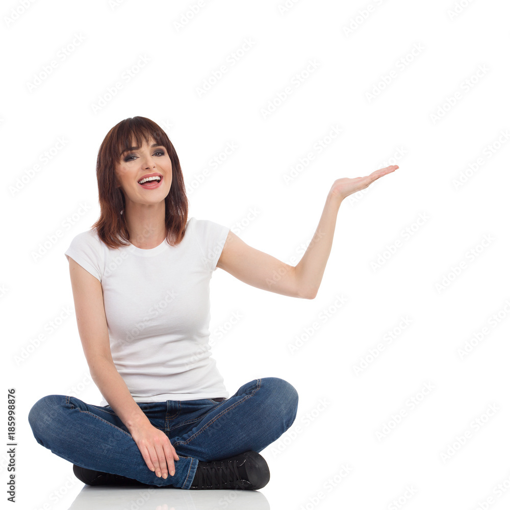 Young Woman Is Sitting Legs Crossed, Holding Hand Raised, Looking At Camera And Talking. Young Woman Is Sitting Legs Crossed, Holding Hand Raised, Looking At Camera And Talking.