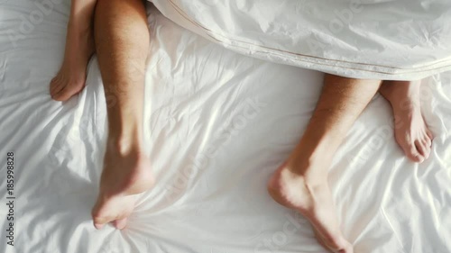 couple in bed making love. male and female legs top view, white linens. sex, 4k