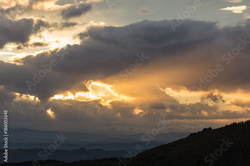 A silhouette of a mountain peak at sunset, beneath sun rays coming out through some clouds