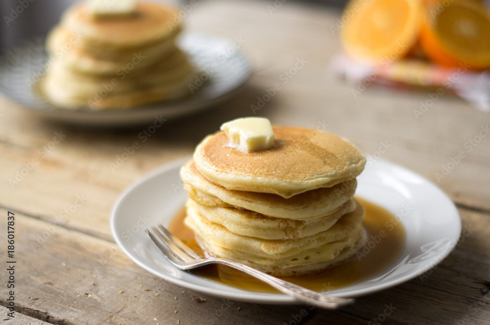 Homemade pancakes with maple syrup and butter on the white plates with oranges on a side, on the wooden table Homemade pancakes with maple syrup and butter on the white plates with oranges on a side, on the wooden table