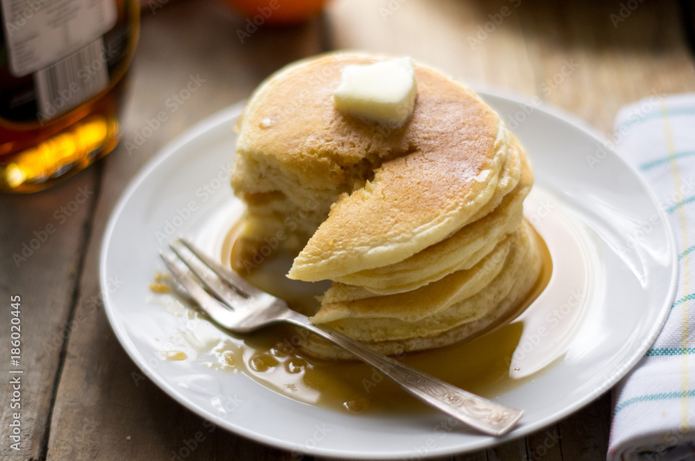 homemade pancakes with maple syrup and butter on the white plate eaten with fork homemade pancakes with maple syrup and butter on the white plate eaten with fork
