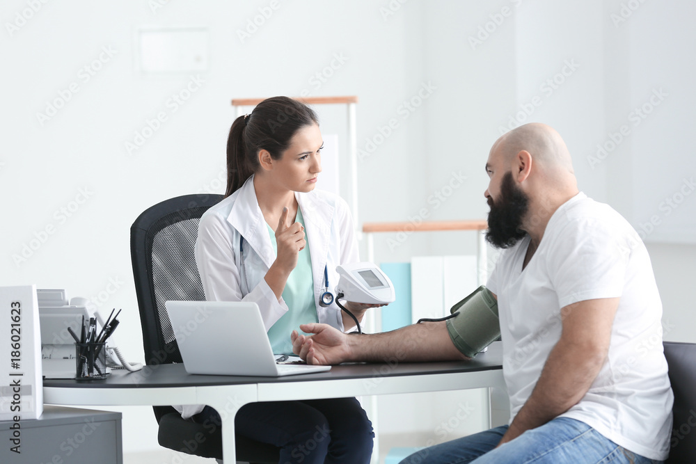 Obraz premium Young female doctor measuring blood pressure of overweight man in clinic