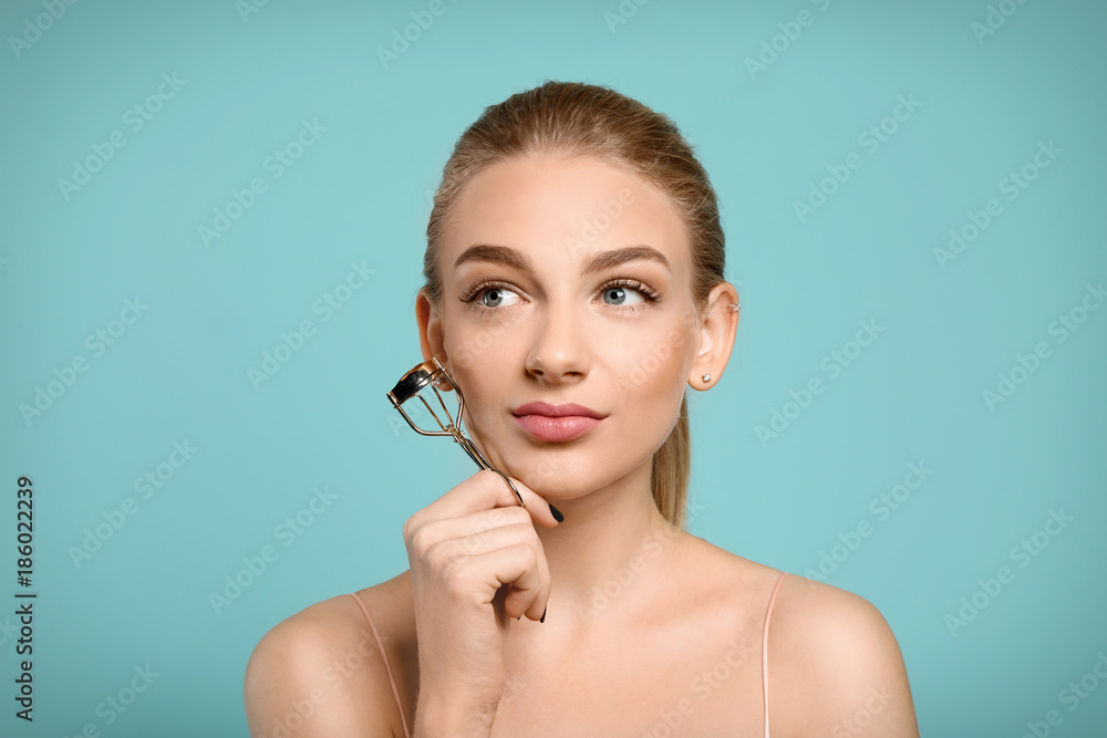 Beautiful young woman with eyelash curler on color background Beautiful young woman with eyelash curler on color background