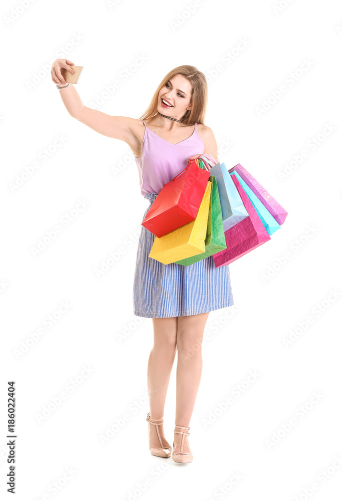 Happy young woman with shopping bags taking selfie on white background