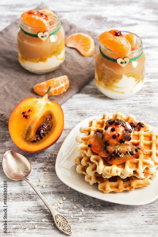 Homemade waffles with cream and pulp tamarillo on a wooden white table. Yogurt with fruit, tangerines, apple puree.