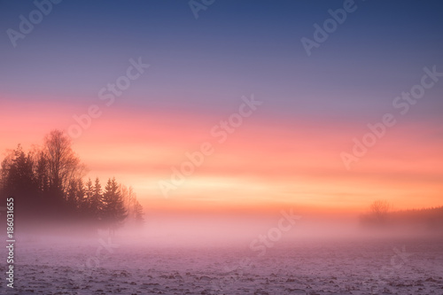 Fototapeta Naklejka Na Ścianę i Meble -  Foggy and colorful sunset with peaceful landscape at winter evening in Finland